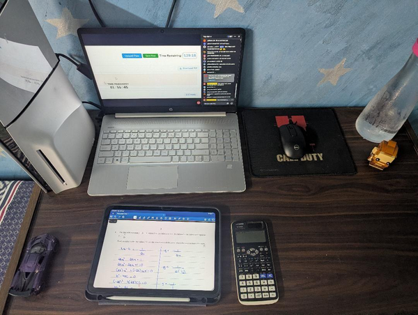 Student desk with online exam submission portal, iPad quadratic equation notes, and calculator